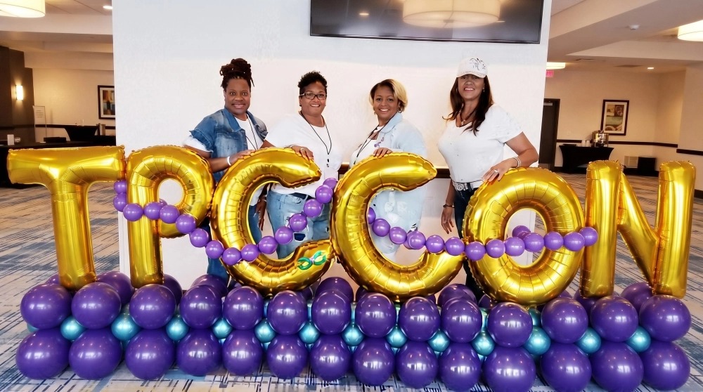 TPCCON attendees posing with large gold balloon letters spelling TPCCON